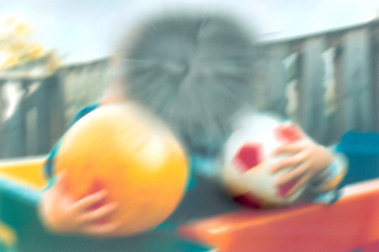A person with a blurred out face (mimicking what a person with AMD would see) holding a yellow ball in one hand and a soccer ball in the other.