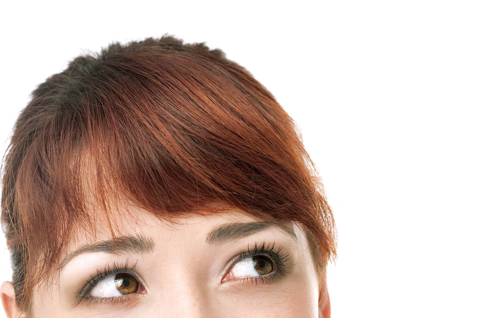 The upper half of the head of a red-headed woman with bangs and brown eyes looking off to the right.