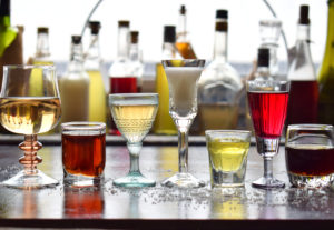 Various alcoholic drinks in glasses lined up on a bar.