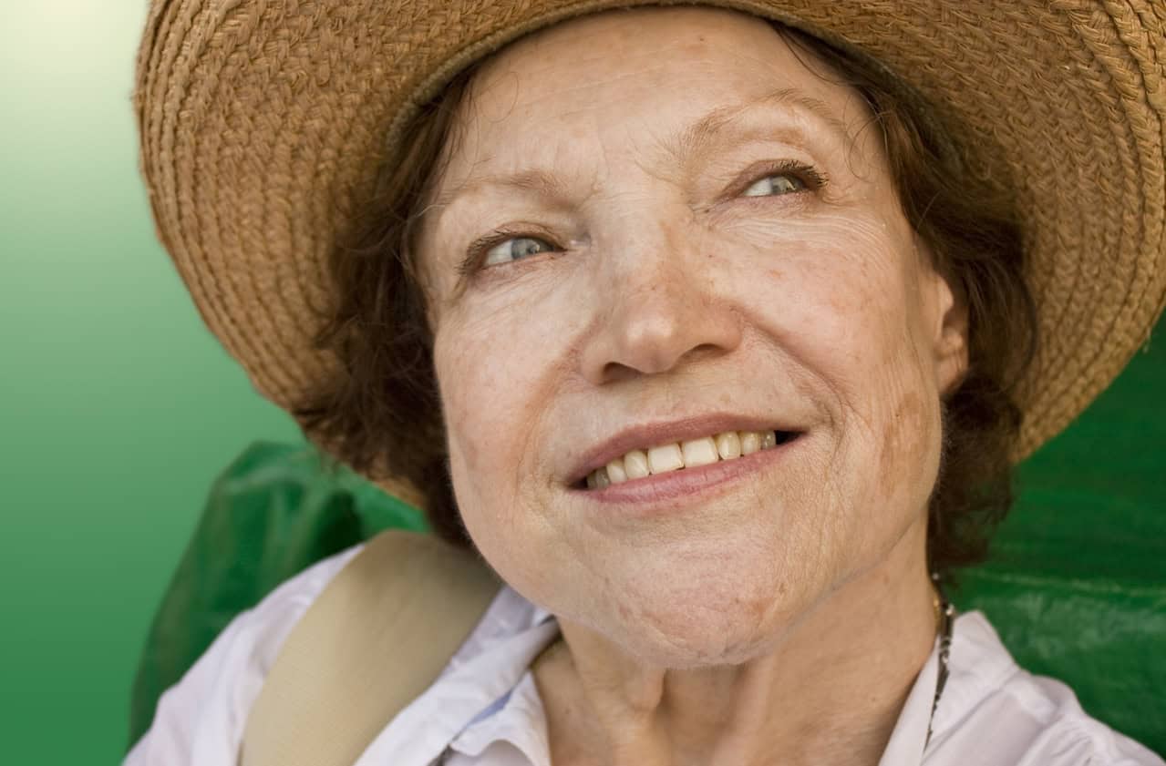 An older woman wearing a straw hat looking happily off to her left.