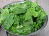 A freshly washed stainless steal bowl of spinach sitting on a grey countertop.