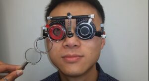 A man with trial frame glasses covering his eyes is tested for astigmatism.