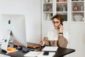 Woman working from home in front of computer and talking on the phone.