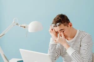 A man wearing a striped shirt sitting at his work station rubbing his eyes due to digital eye strain.