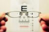 A person holding eye glasses in front of a snelling chart.