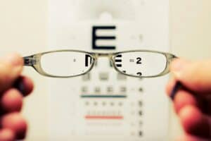 A person holding eye glasses in front of a snelling chart.
