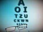 A pair of glasses looking at the bottom row of a snellen chart through one lens.